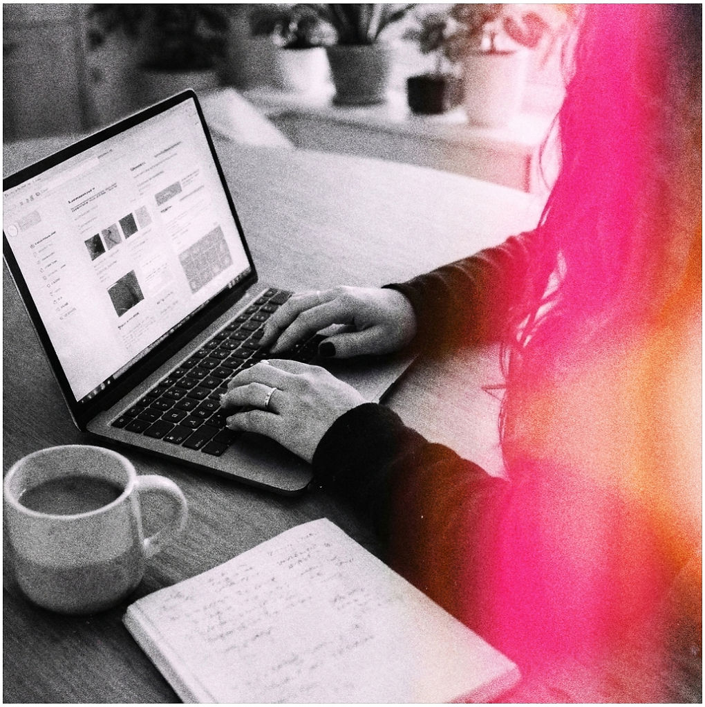 Hands working on a laptop beside a notebook and coffee, with a pink and orange light leak